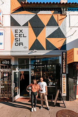 Lea and Andre Higginbotham, owners of Excelsior Coffee, cannot help but be all smiles as they stand in front of their business on a bright sunny day.