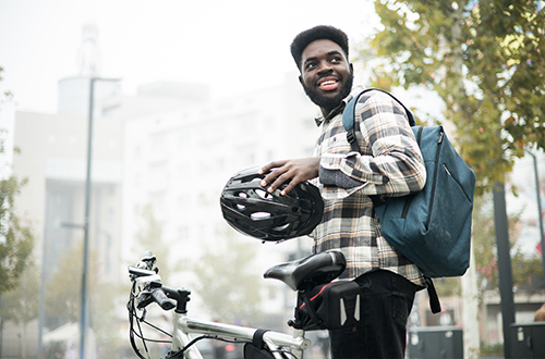 Un hombre negro ajusta su casco junto a su bicicleta eléctrica