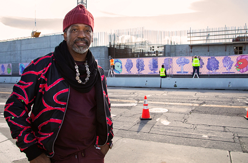 Artist Malik Seneferu standing on sidewalk with his mural in the background