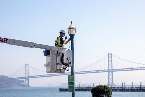 la luz de la calle está siendo reparada con el Puente de la Bahía en el fondo