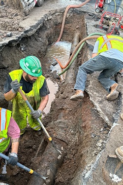 Los equipos bombean agua para sacarla de una tubería principal rota y excavan para descubrir la tubería.