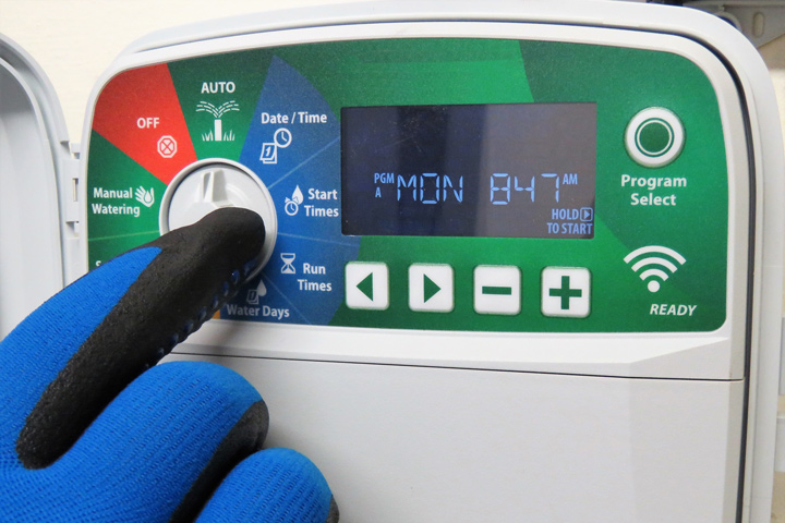 Person with gardening glove on setting the timer on an irrigation controller.