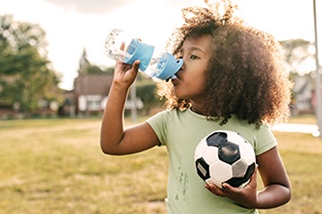 Niño de pelo rizado sosteniendo una pelota de fútbol y bebiendo de una botella de agua