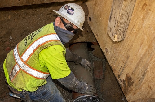 trabajador en una zanja sosteniendo un lateral de alcantarillado