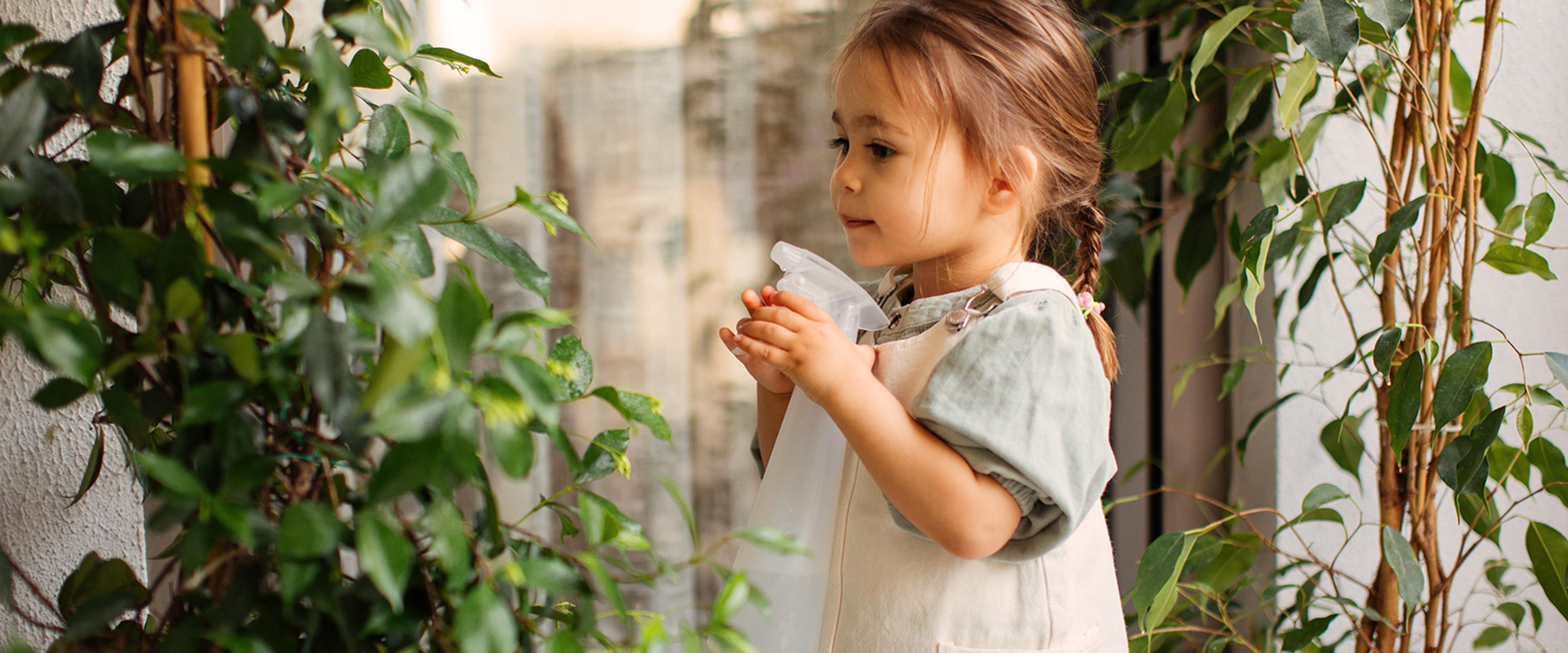 Niña regando plantas con una botella de spray.