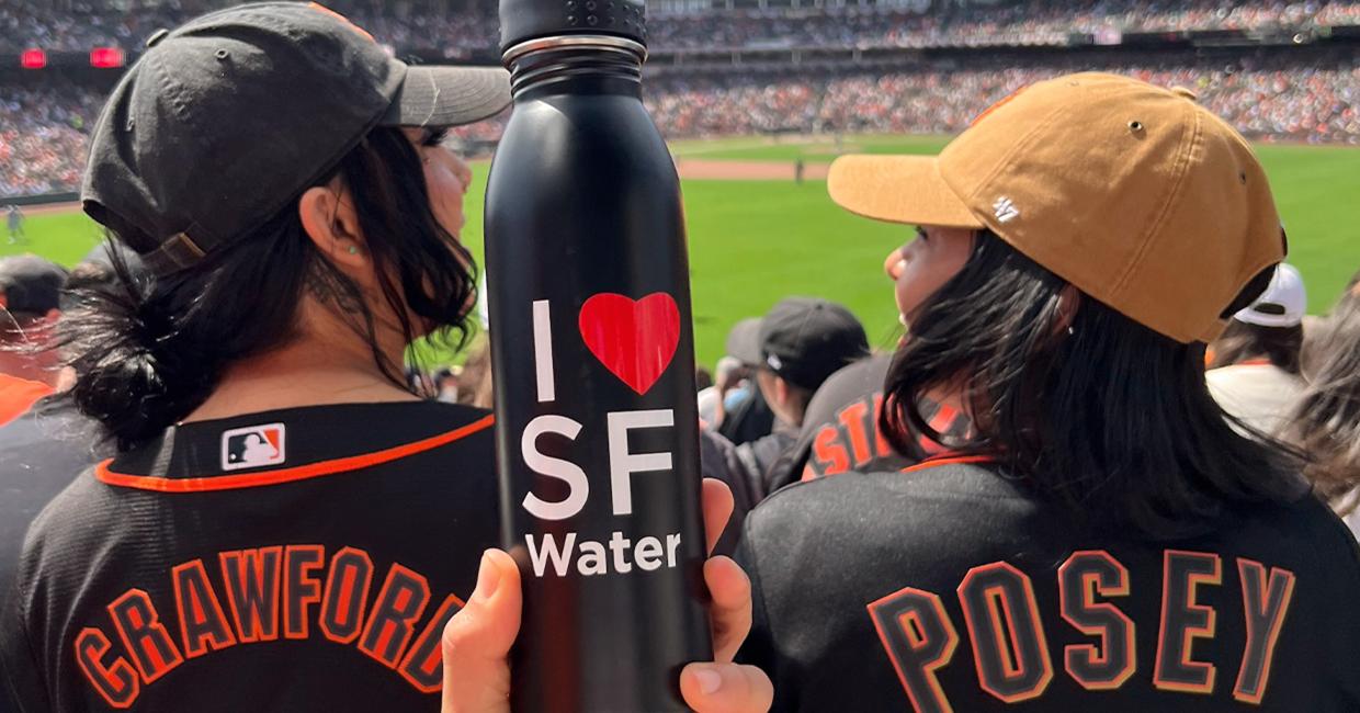 Two SF Giants fans at a baseball game and SF water bottle in foreground.