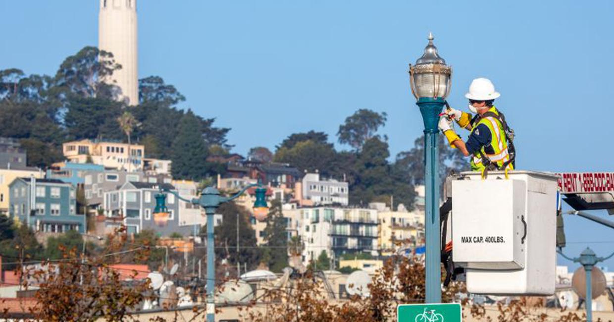 SFPUC worker and light pole with San Francisco in the background