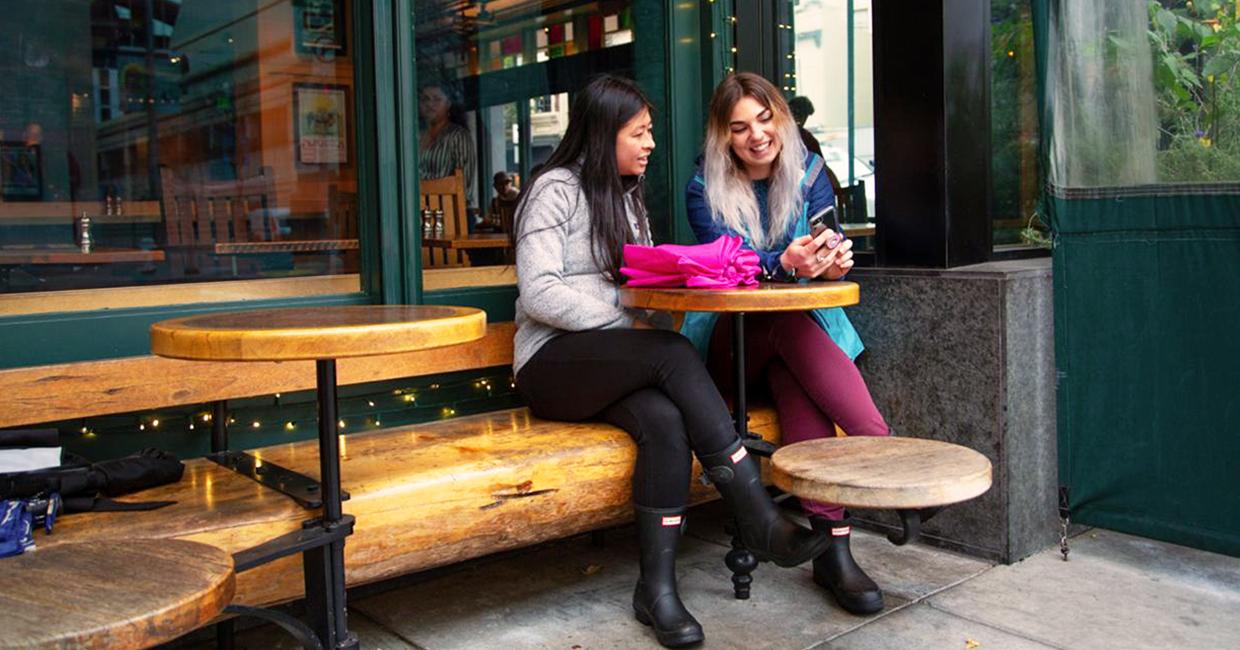 Two people sit outside a business talking.