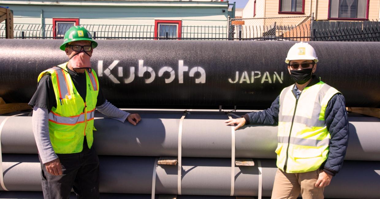 Two people standing in front of large pipes.