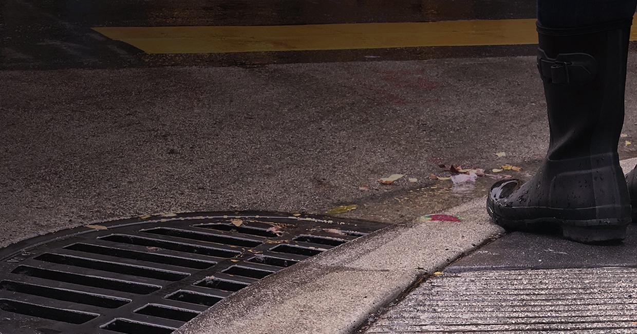 Person in black rainboots standing next to cleared storm drain