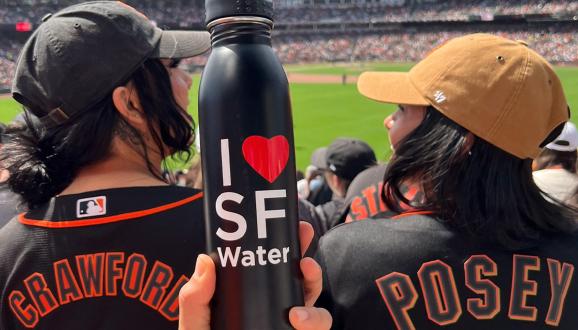 Two people holding an I love SF Water water bottle at SF Giants game