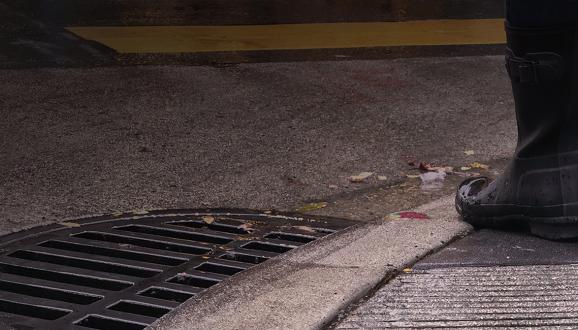 Person in black rainboots standing next to cleared storm drain